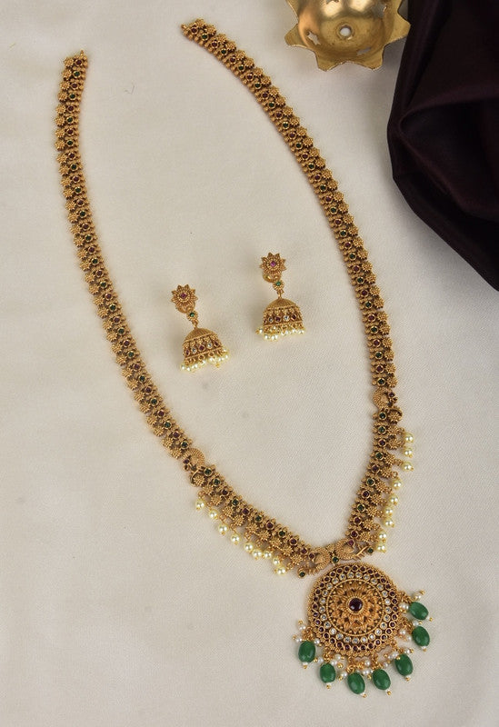 A traditional gold necklace set with intricate designs, featuring a large pendant adorned with green stones and pearl drops. The set includes matching jhumka earrings with similar detailing.