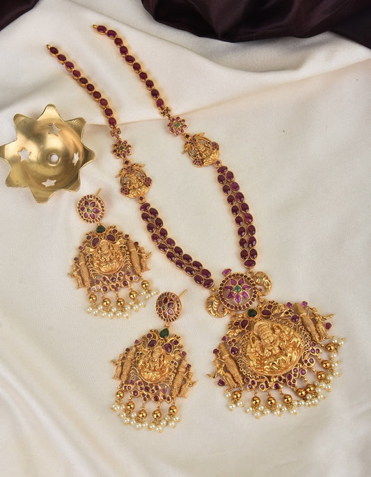 A set of traditional gold jewelry with intricate designs, including a necklace and matching earrings adorned with red and green gemstones and pearl accents.