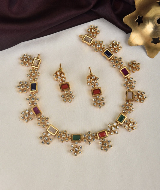 A gold jewelry set consisting of a necklace and matching earrings, adorned with colorful gemstones and intricate floral designs.