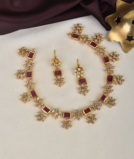 A gold jewelry set consisting of a necklace and matching earrings, adorned with red square gemstones and clusters of small white stones.