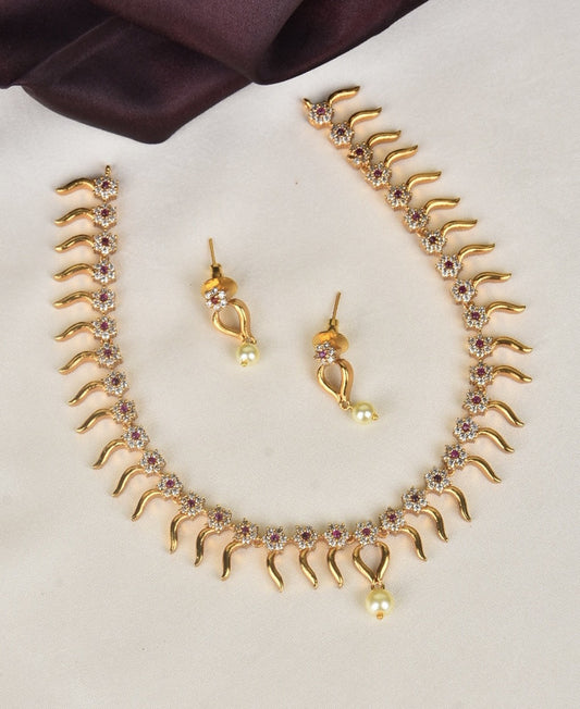 A gold necklace with a wavy design, adorned with small colorful gemstones and matching earrings featuring a similar wavy design and pearl drops.