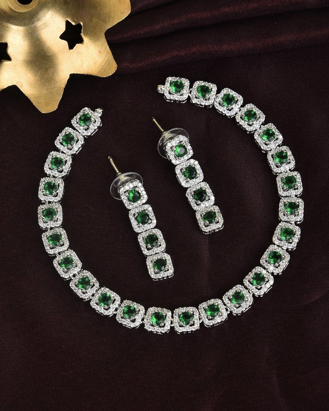 A jewelry set featuring a necklace and a pair of earrings, each adorned with square green gemstones surrounded by smaller clear stones.