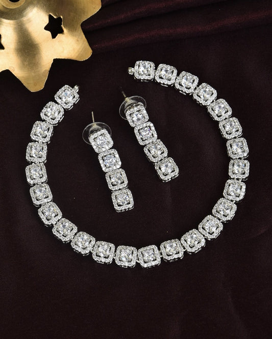 A set of silver jewelry featuring a bracelet and a pair of dangling earrings, each adorned with square-shaped, diamond-like stones.