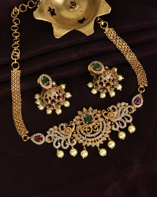 Gold necklace and earrings set with intricate designs, green and red gemstones, and pearl accents.