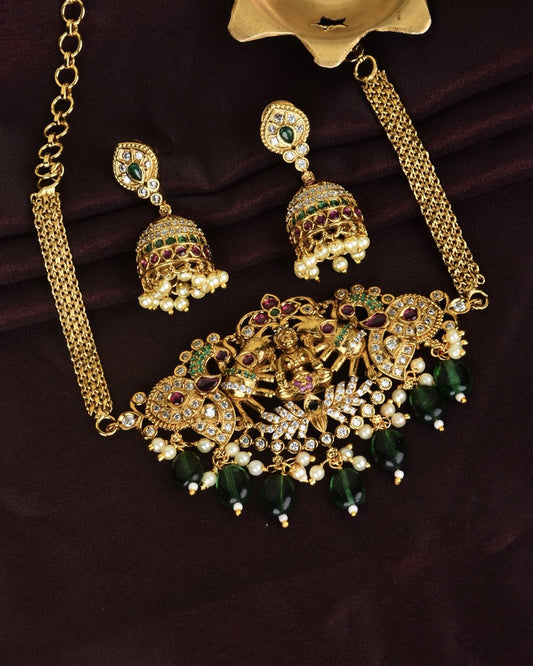 A set of gold-toned jewelry featuring a necklace with intricate designs, green and white beads, and matching earrings adorned with green and white stones.