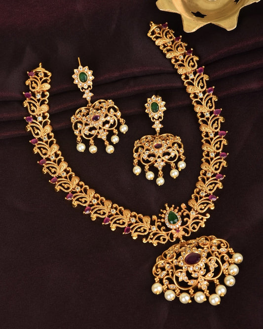 A set of ornate gold jewelry consisting of a necklace and matching earrings, adorned with green and red gemstones and pearl accents.