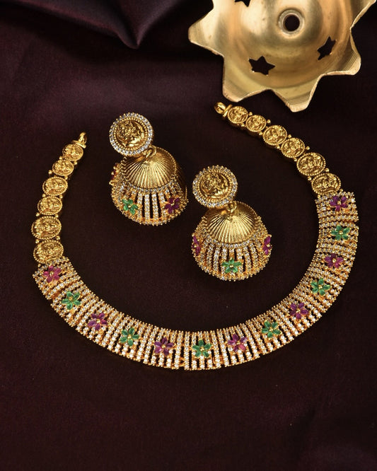 A gold necklace and matching earrings with intricate designs, featuring green and purple gemstones.