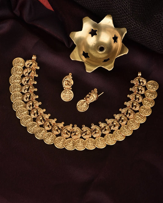 Gold coin necklace and matching earrings set on a dark fabric background.