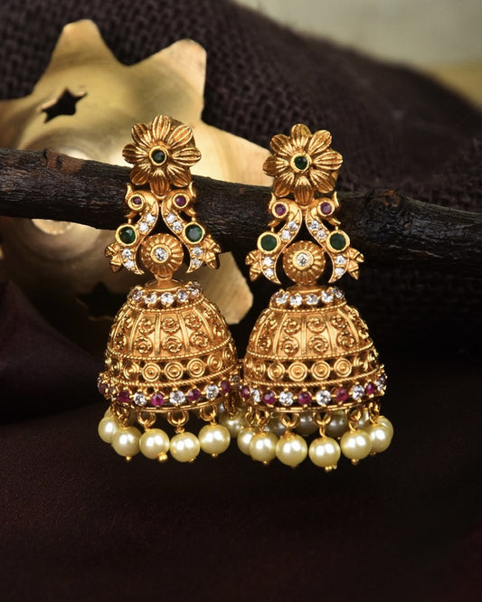 Gold jhumka earrings with intricate floral design, studded with green and red gemstones, and adorned with pearl drops.