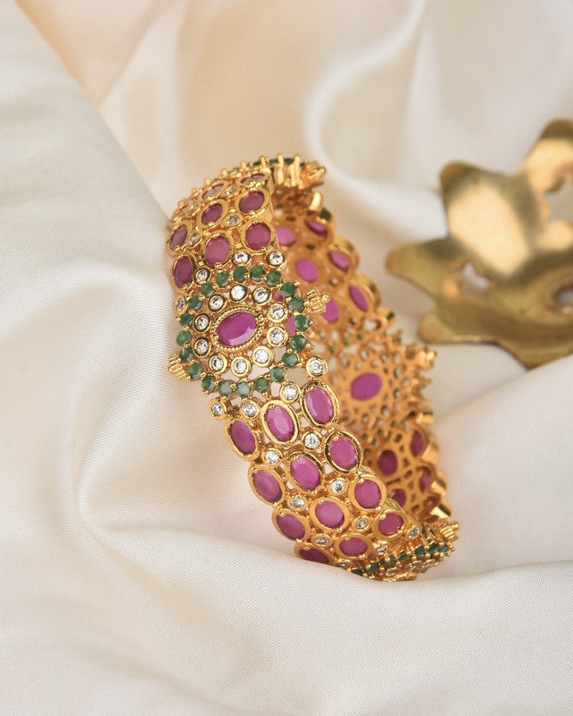 Gold bracelet adorned with pink and green gemstones.