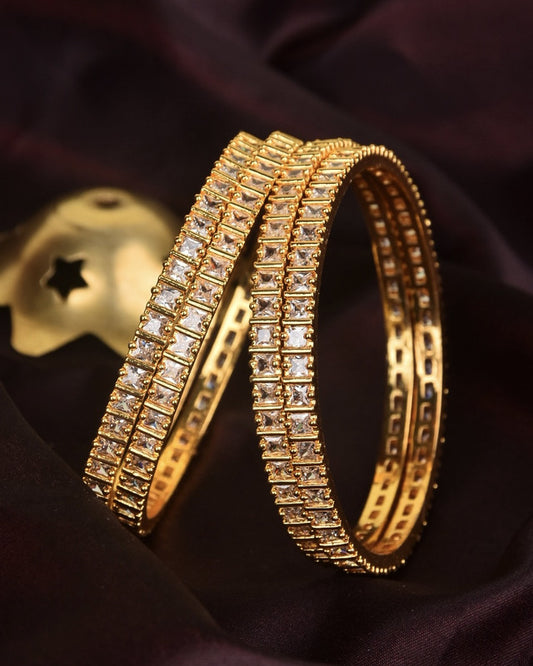 Two gold bangles adorned with square-cut clear stones.