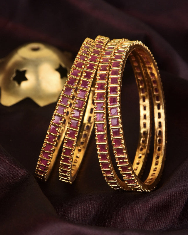 Four gold bangles with embedded red stones.