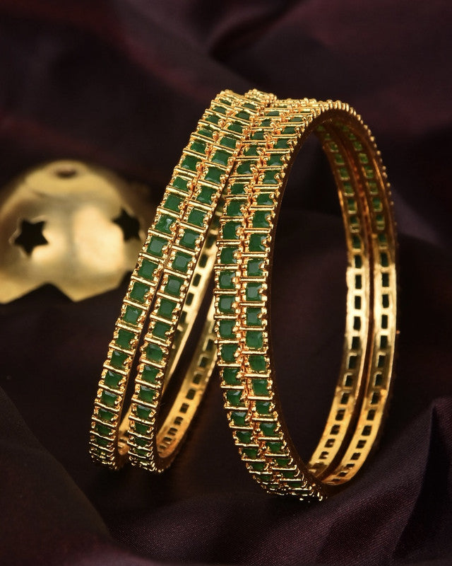 Two gold bangles adorned with green gemstones.