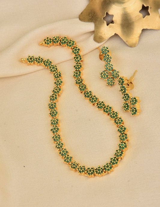 A gold necklace and matching earrings adorned with small green floral designs.