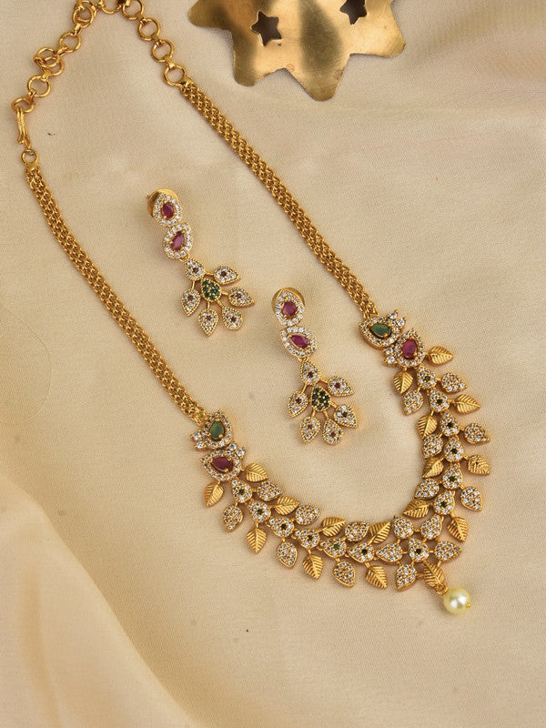 A gold necklace with intricate leaf designs and matching earrings, adorned with colorful gemstones and a single pearl pendant.