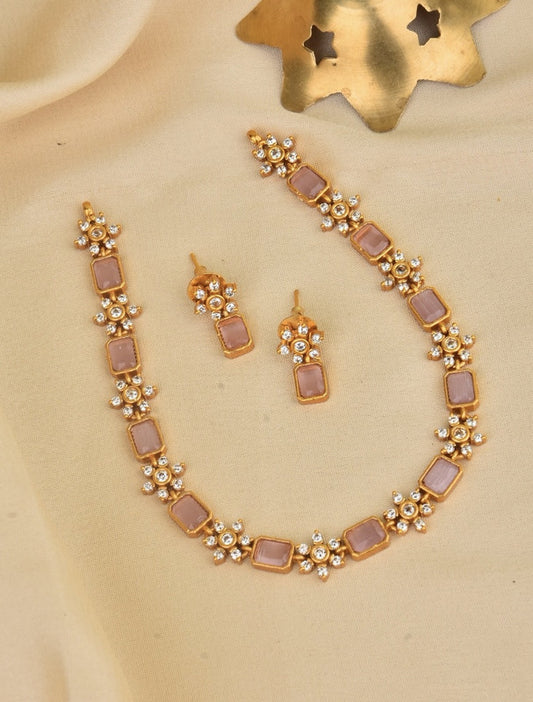 A gold necklace and matching earrings set with rectangular pink stones and small white pearls.