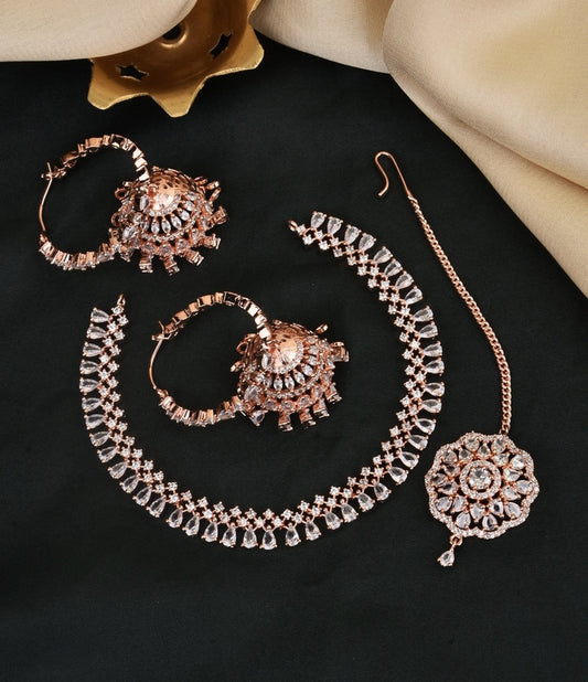 A set of rose gold jewelry including a pair of hoop earrings with intricate designs, a choker necklace adorned with clear stones, and a maang tikka with a floral pattern.