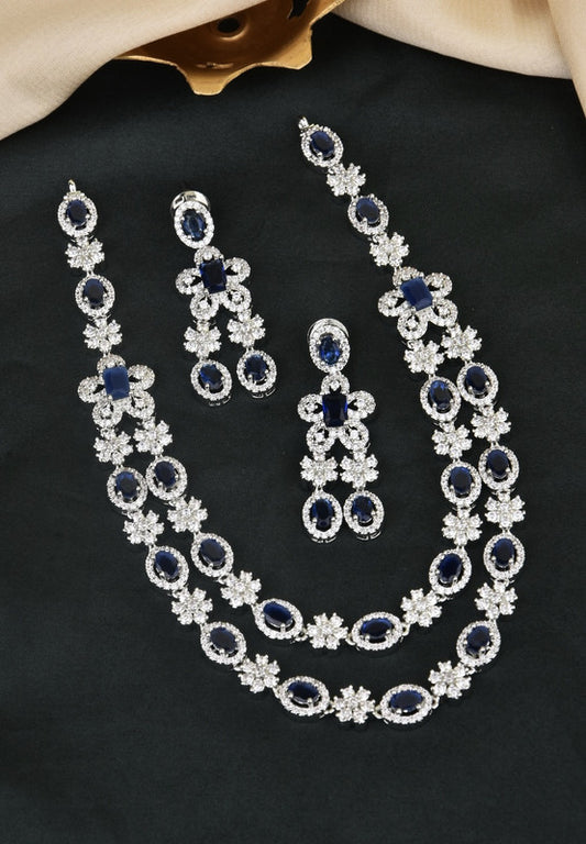 A jewelry set consisting of a necklace, a pair of earrings, and a bracelet, all featuring blue gemstones surrounded by clear crystals.