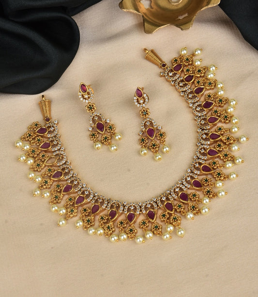 A gold necklace and matching earrings set adorned with red and white stones and pearl accents.