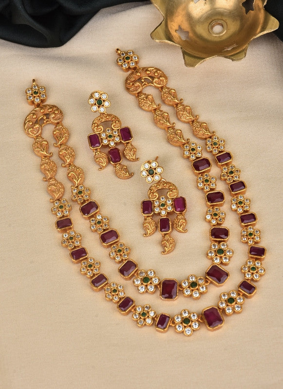 A set of traditional gold jewelry consisting of a necklace and matching earrings. The necklace features intricate gold designs with red gemstones and white pearls. The earrings have a similar design with red gemstones and white pearls.