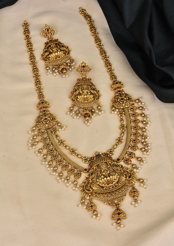 A set of traditional gold jewelry consisting of a long necklace with intricate designs and matching earrings, adorned with small pearls and gemstones.