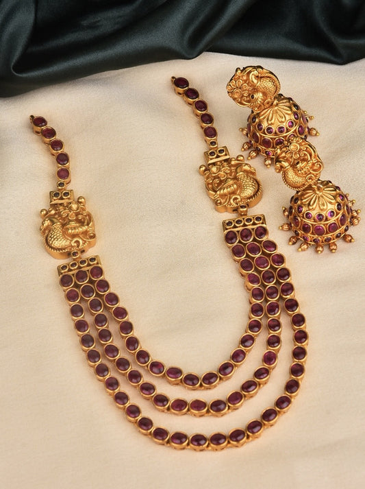 A set of traditional gold jewelry featuring a three-layered necklace with purple gemstones and matching earrings.