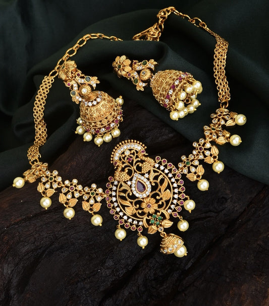 A gold necklace set with intricate designs, adorned with pearls and red gemstones, accompanied by matching earrings.