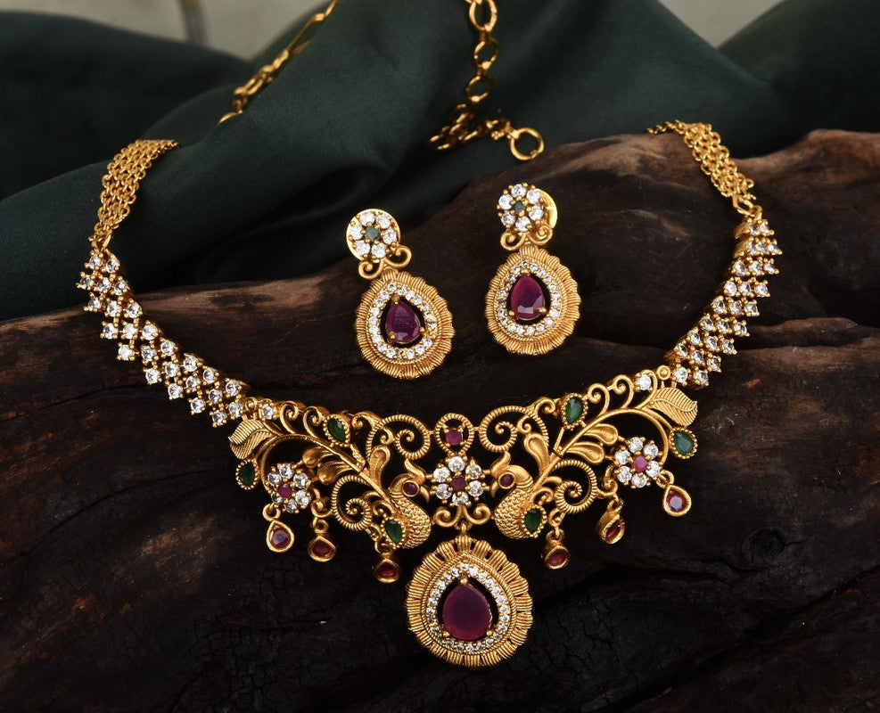 A gold necklace and matching earrings set adorned with intricate designs, red gemstones, and white crystals.