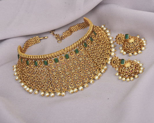 Gold choker necklace with intricate filigree design, green gemstones, and pearl accents, accompanied by matching earrings.