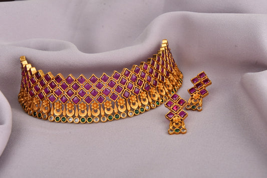 A gold choker necklace with a geometric pattern featuring purple and green gemstones, accompanied by matching earrings.