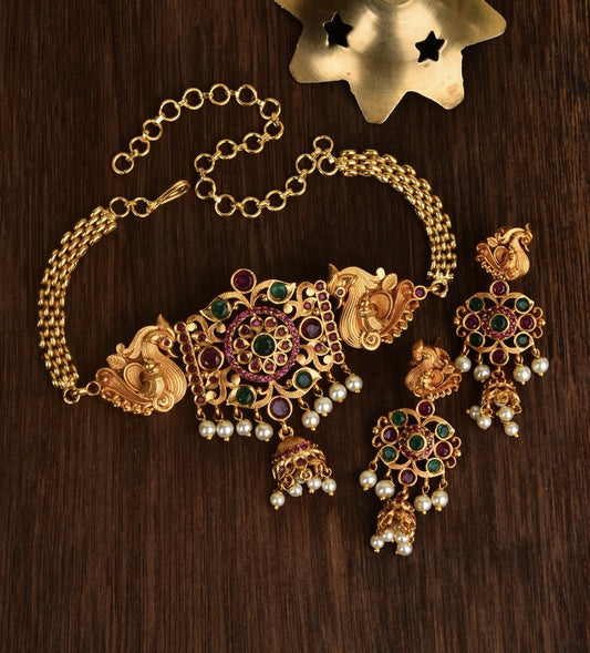 A set of traditional gold jewelry featuring a necklace and matching earrings adorned with intricate designs, colorful gemstones, and pearl accents.