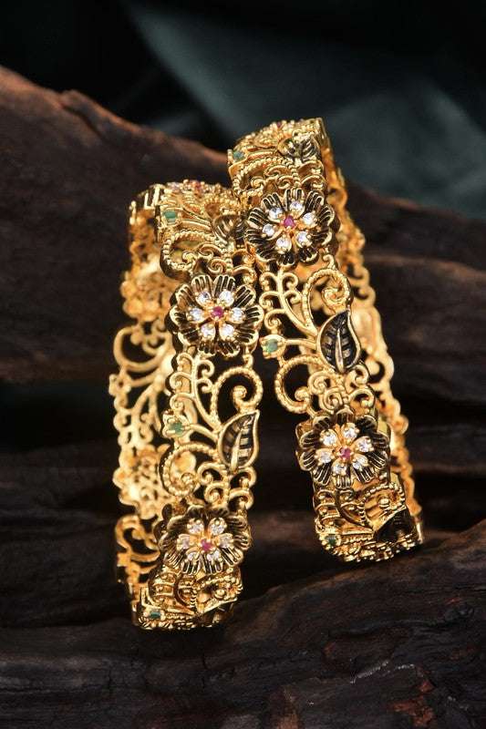 Two intricately designed gold bangles with floral and leaf patterns.