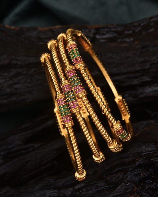 Gold bangles with intricate designs and embedded green and pink gemstones.