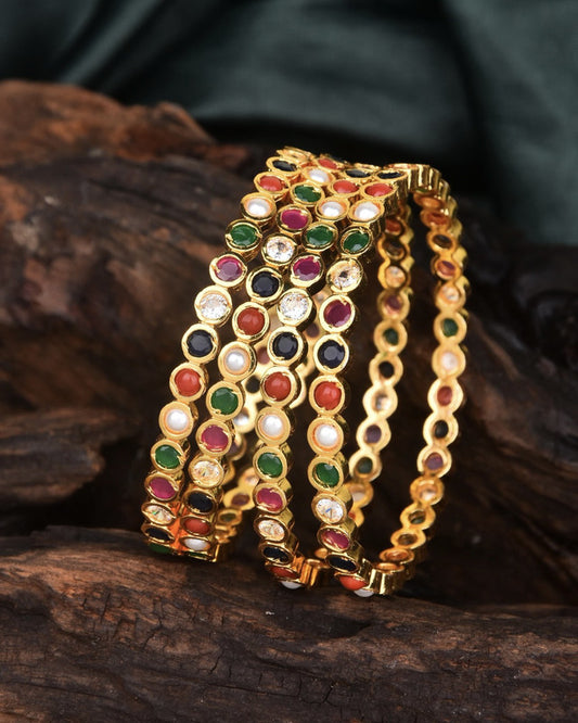 Three gold bangles adorned with multicolored gemstones.