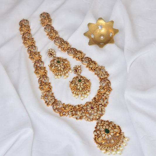 A set of ornate gold jewelry including a necklace, a pair of earrings, and a maang tikka, all adorned with intricate designs and embedded with gemstones.