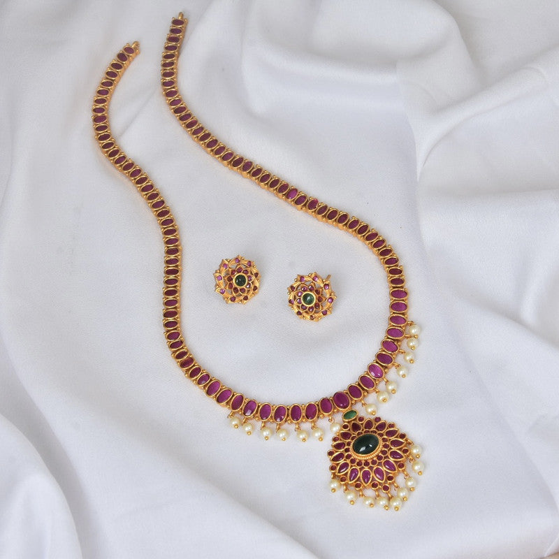 A gold necklace set with red and green gemstones, accompanied by matching earrings, displayed on a white fabric background.