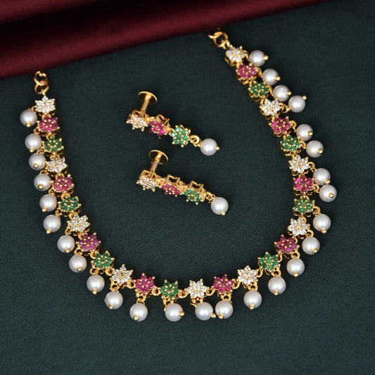 A gold necklace and matching earrings adorned with white pearls, green, pink, and white gemstones arranged in floral patterns.