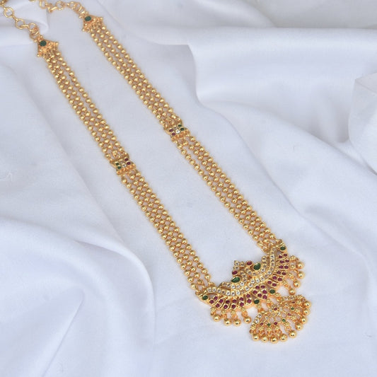 A gold necklace with intricate designs and embedded colorful gemstones, displayed on a white fabric.