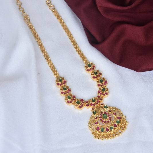 A gold necklace with intricate designs featuring green and red gemstones.