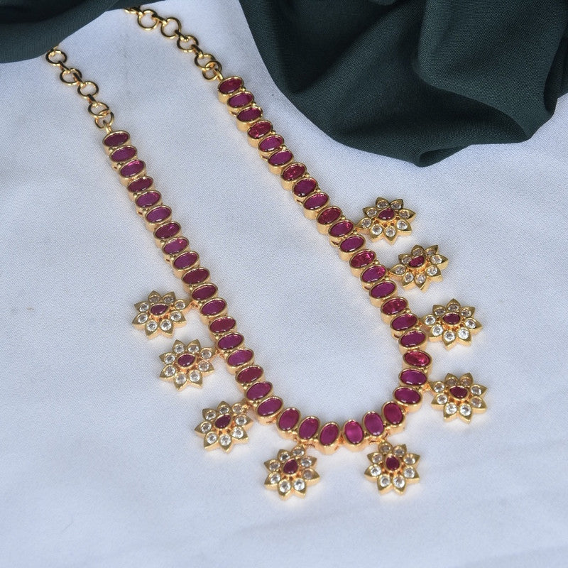 A gold necklace with red gemstones and floral-shaped pendants adorned with smaller white stones.