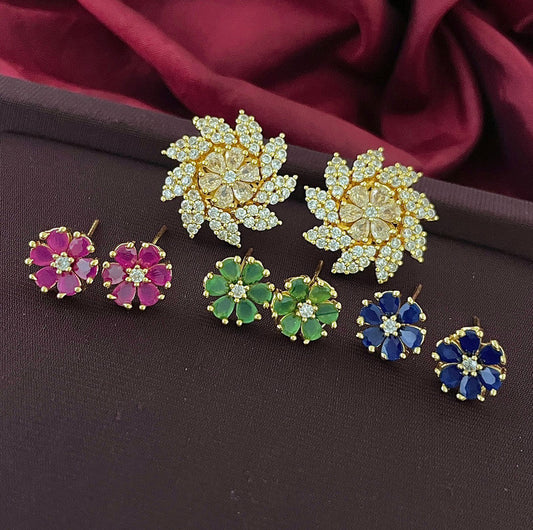 Three pairs of floral-shaped earrings with different colored gemstones: one pair with white stones, one pair with pink stones, one pair with green stones, and one pair with blue stones.